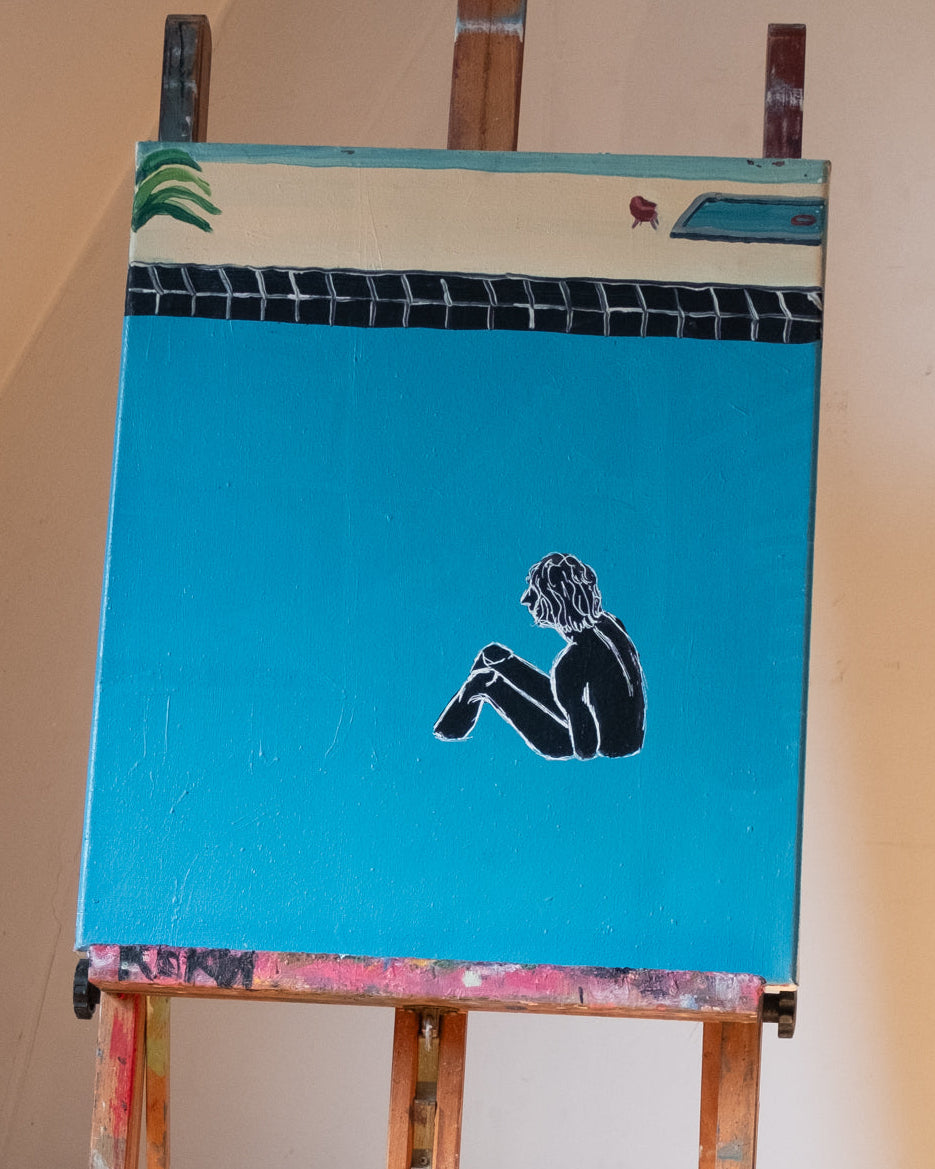 Painting of a person sitting on a blue background on an easel.