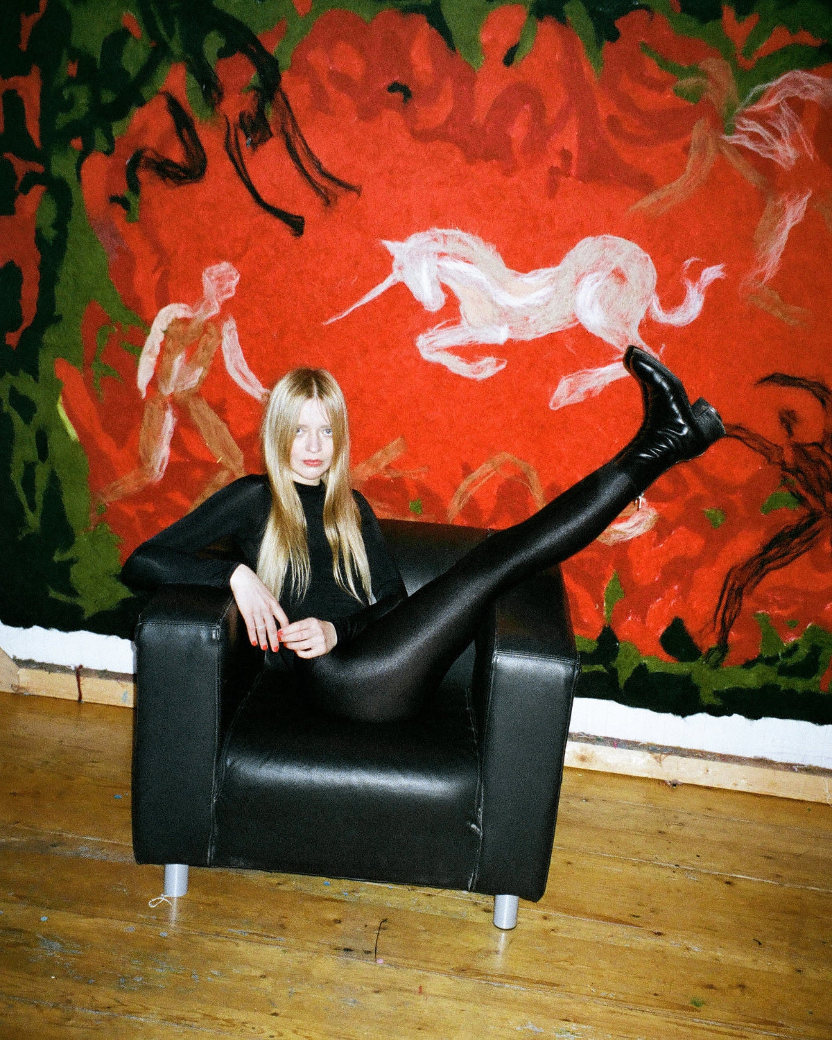 Person sitting on a black chair in front of a vibrant tapestry with red and green colors.