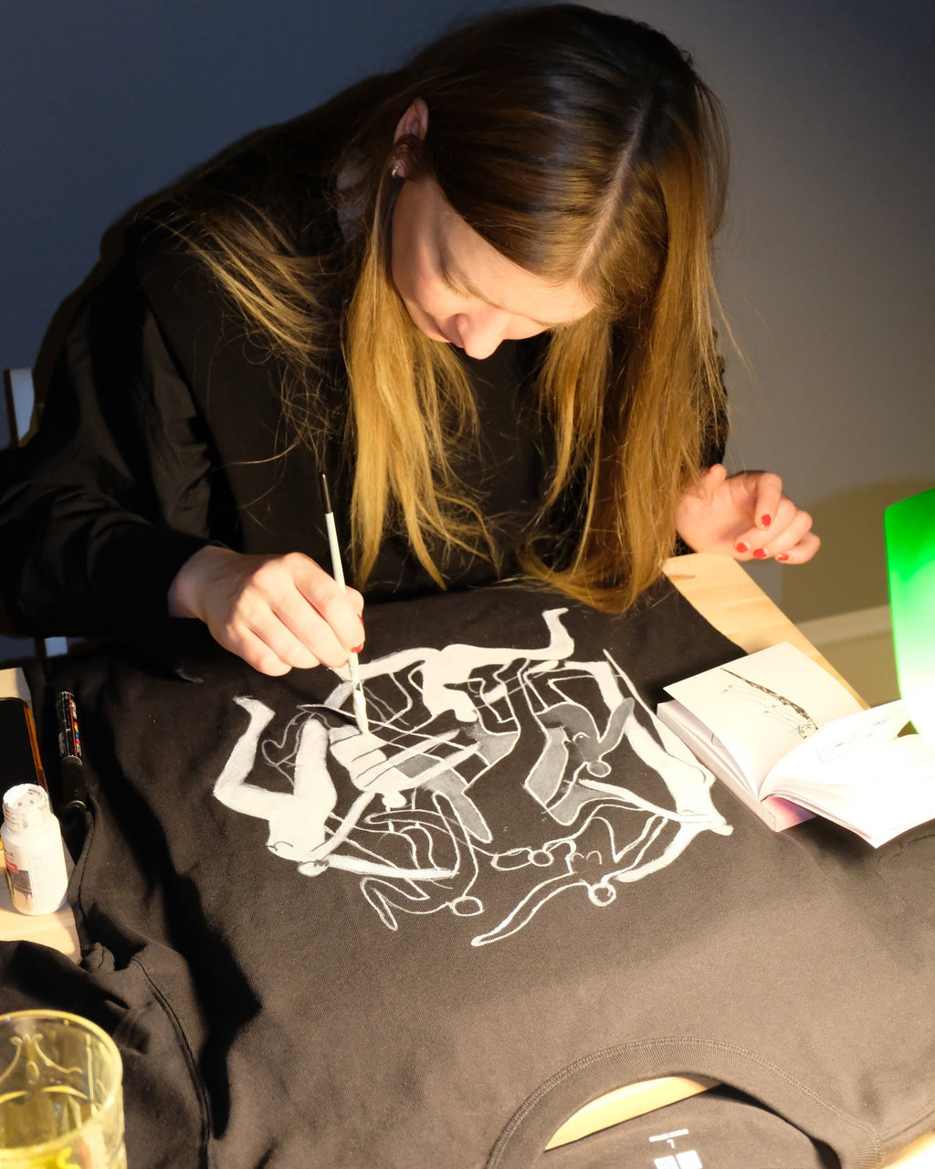 Person hand painting on a black t-shirt with white graphics in a casual setting.