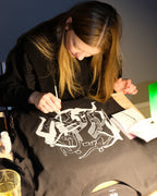 Person hand painting on a black t-shirt with white graphics in a casual setting.