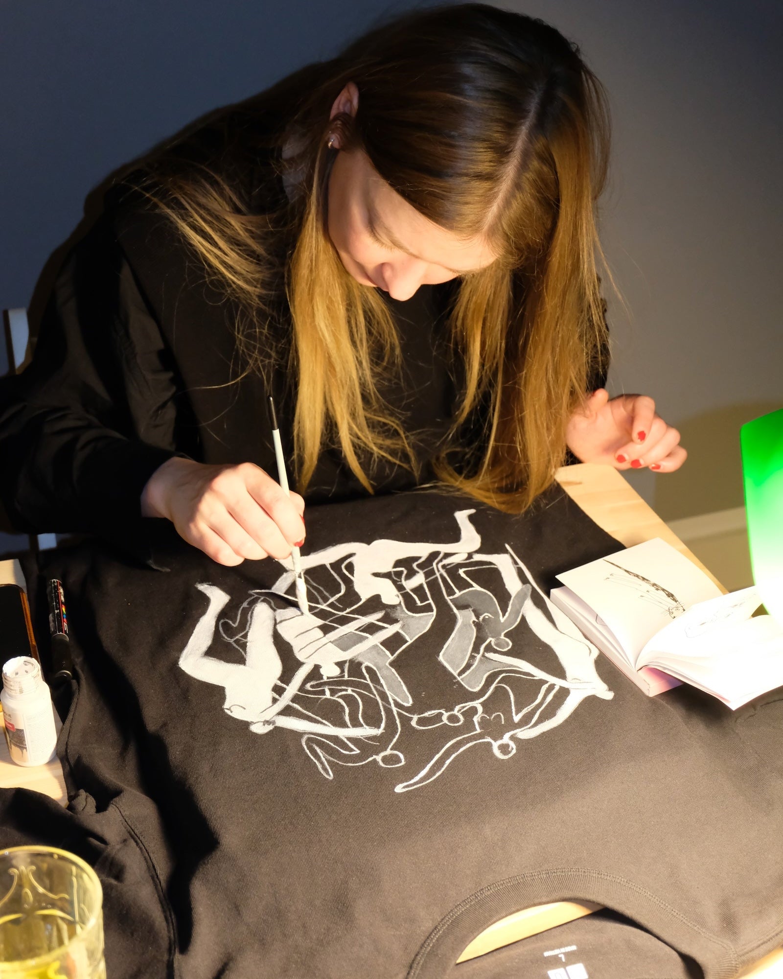 Person hand painting on a black t-shirt with white graphics in a casual setting.