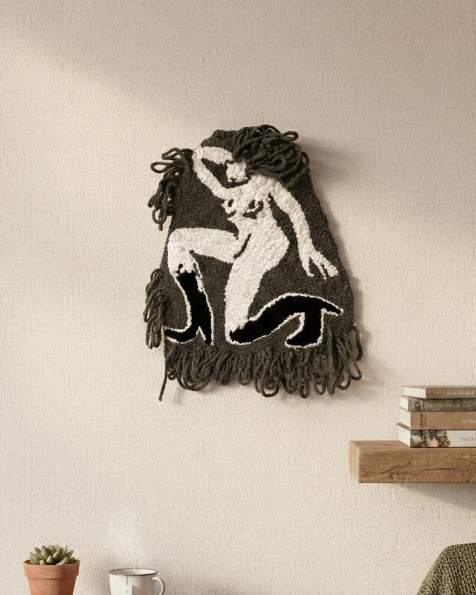 Woven wall art of a nude figure on a beige wall with wooden shelves below.